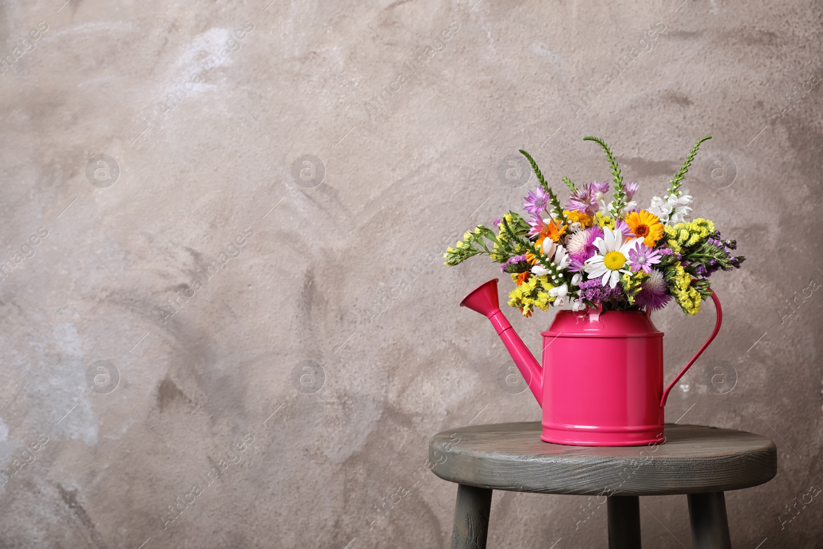 Photo of Watering can with beautiful wild flowers on table against grey background