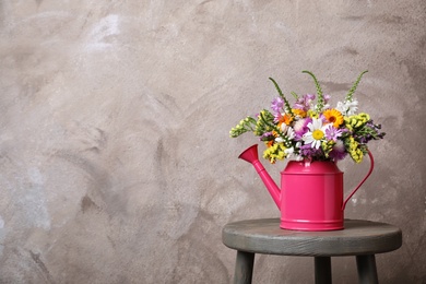 Photo of Watering can with beautiful wild flowers on table against grey background