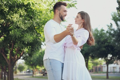 Lovely young couple dancing together in park on sunny day