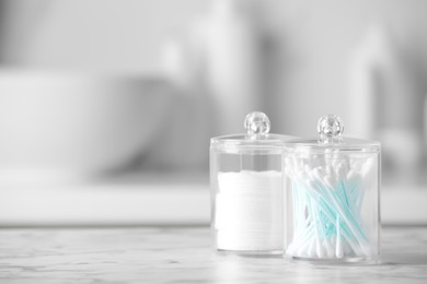 Photo of Plastic jars with cotton pads and swabs on white countertop in bathroom. Space for text