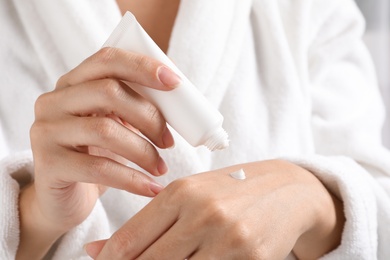 Photo of Woman in bathrobe applying moisturizing hand cream, closeup. Winter skin care cosmetic