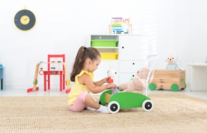 Cute little girl playing with toy walker and teddy bear at home