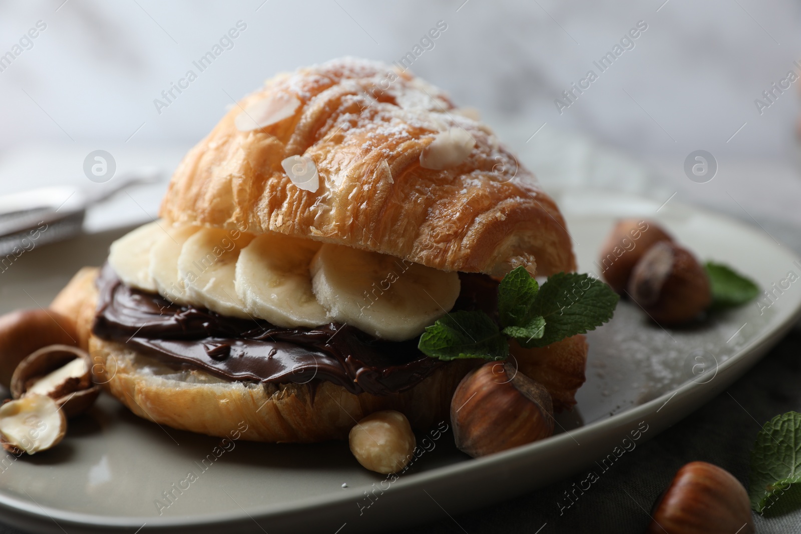 Photo of Delicious croissant with banana, chocolate and hazelnuts on plate, closeup