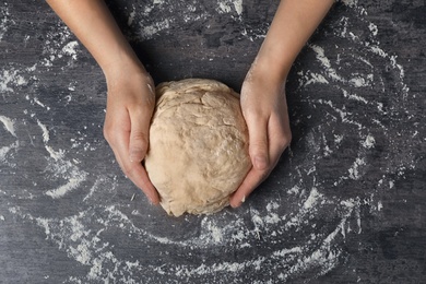 Photo of Young woman kneading dough at table, top view