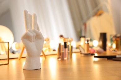 Photo of Ring hand holder and different cosmetic products on wooden dressing table in makeup room, selective focus