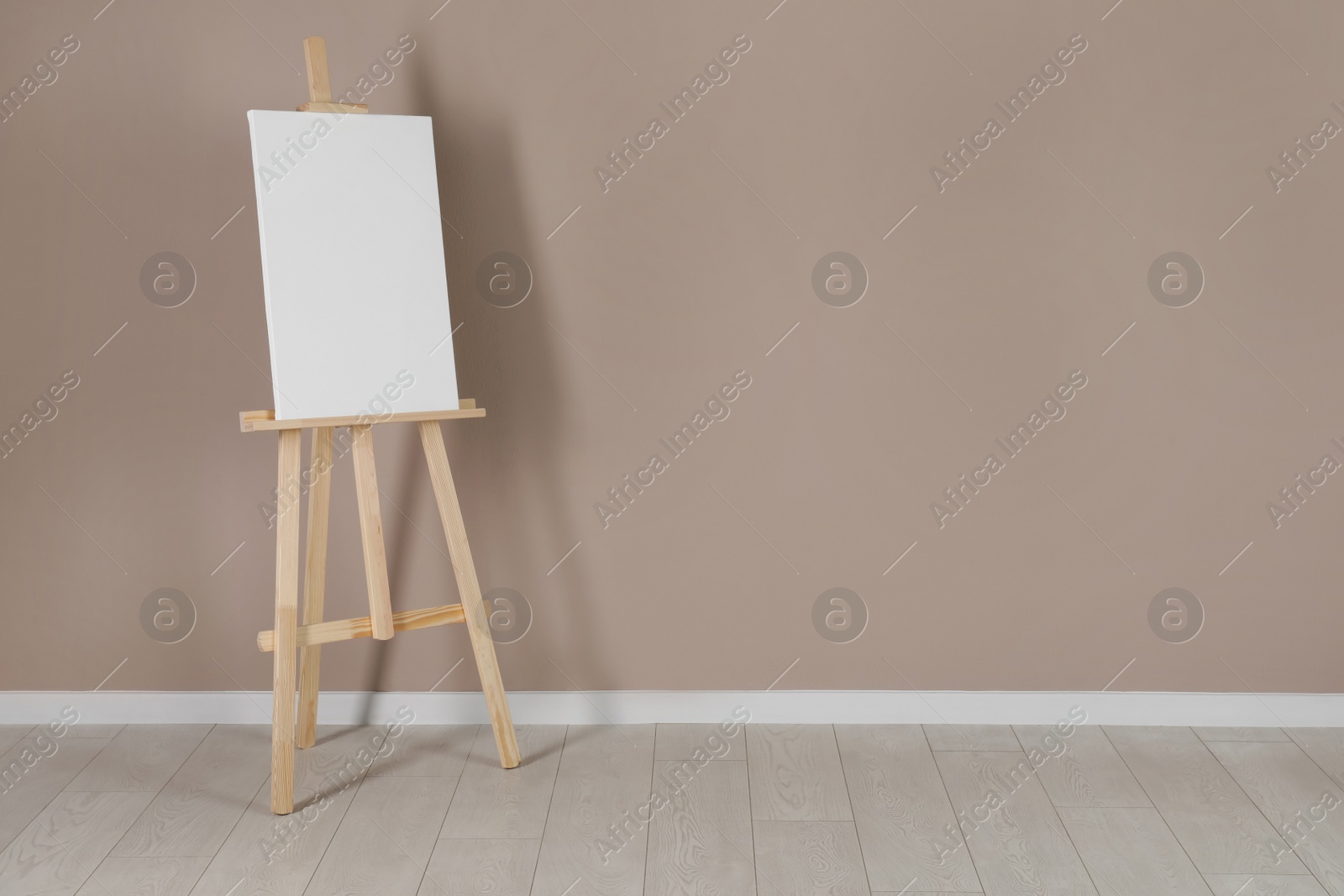 Photo of Wooden easel with blank canvas near beige wall. Space for text