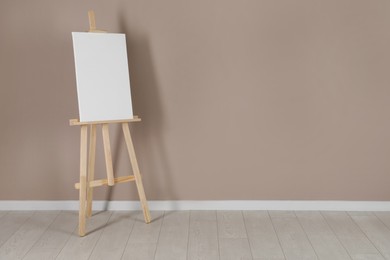 Photo of Wooden easel with blank canvas near beige wall. Space for text