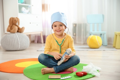 Cute child imagining himself as doctor while playing with stethoscope and toy bear at home