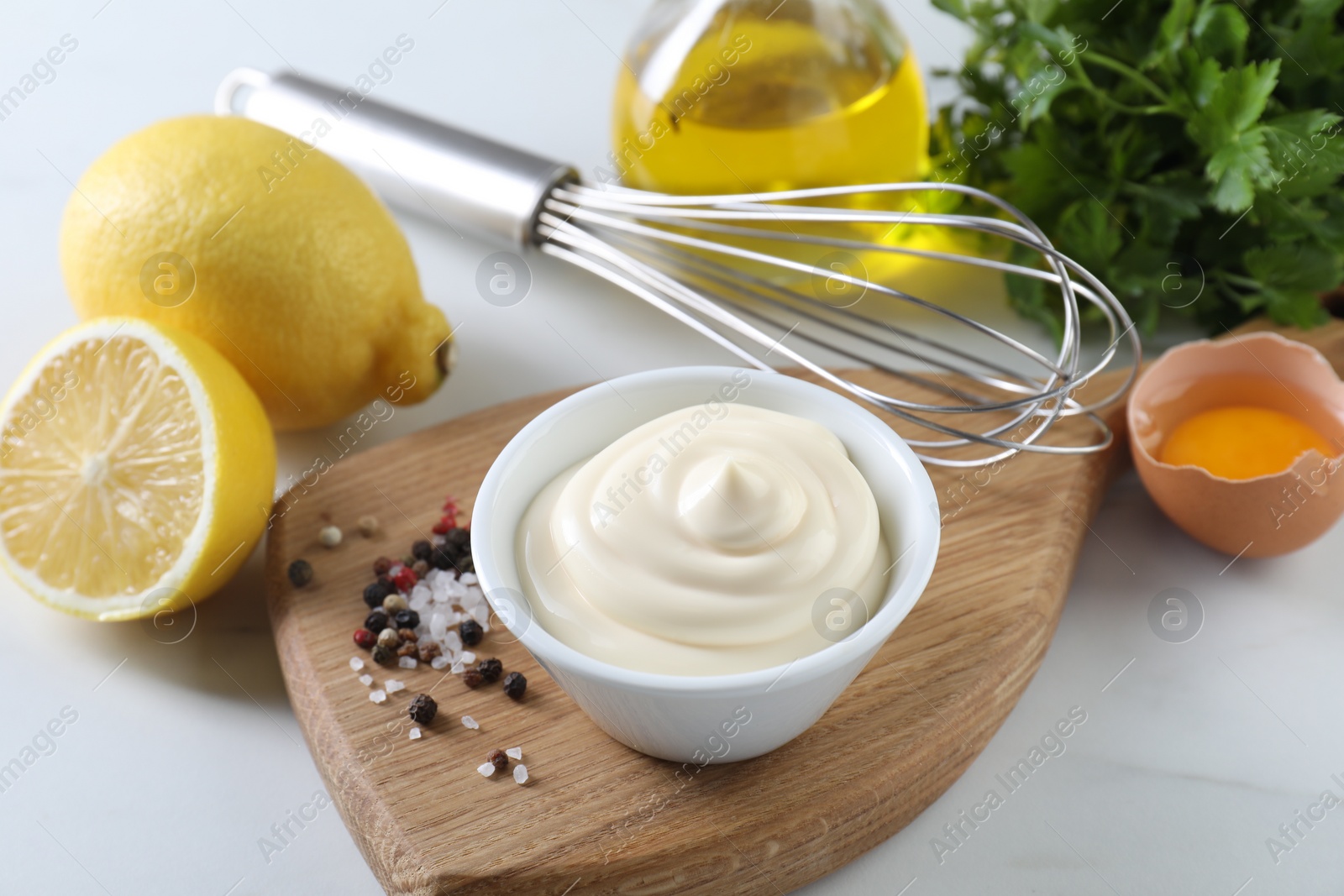 Photo of Tasty mayonnaise sauce in bowl, ingredients and spices on white table, closeup