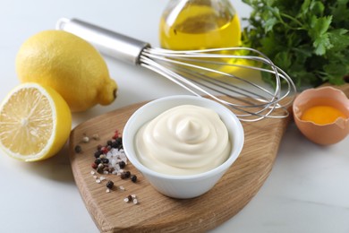 Photo of Tasty mayonnaise sauce in bowl, ingredients and spices on white table, closeup