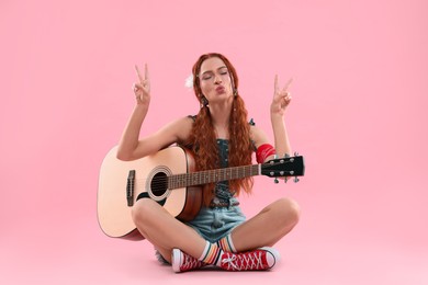 Photo of Stylish young hippie woman with guitar showing V-sign on pink background