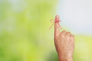 Photo of Man showing index finger with tied bow as reminder on green blurred background, closeup. Space for text