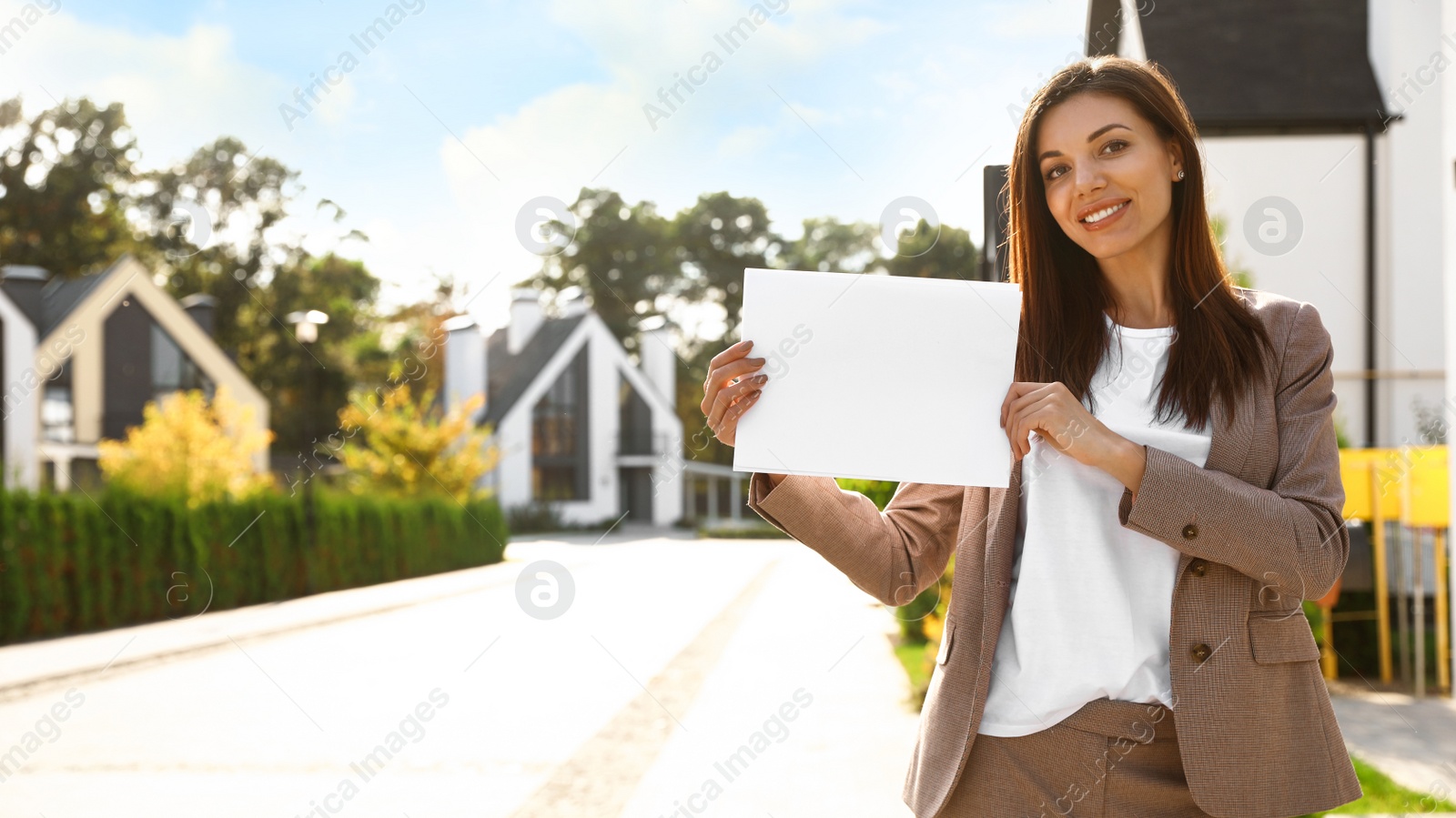 Photo of Beautiful agent holding real estate sign outdoors