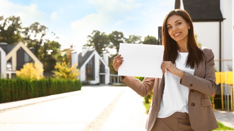 Photo of Beautiful agent holding real estate sign outdoors