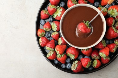 Photo of Fondue fork with strawberry in bowlmelted chocolate surrounded by different berries on light table, top view