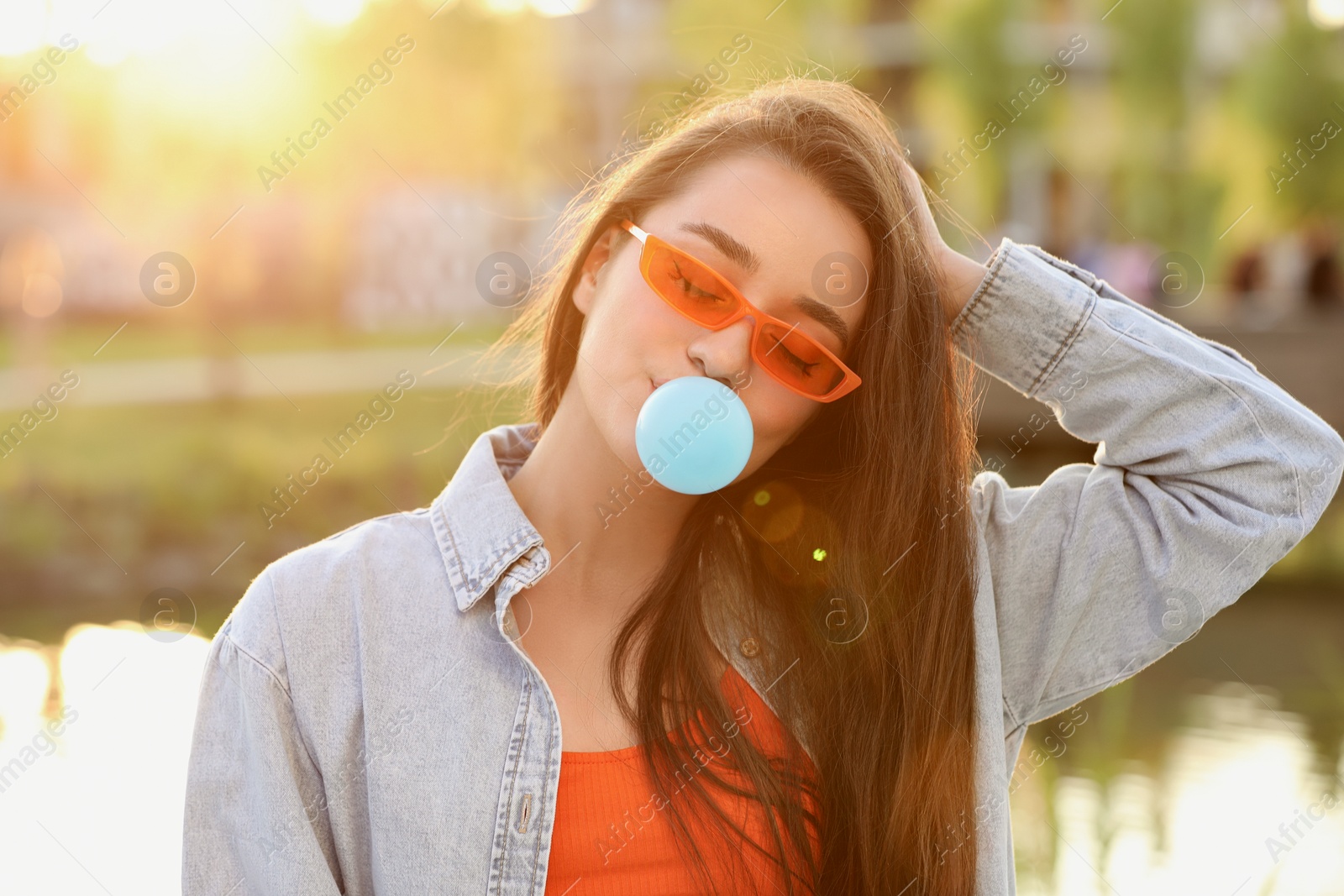 Photo of Beautiful young woman in sunglasses blowing bubble gum outdoors