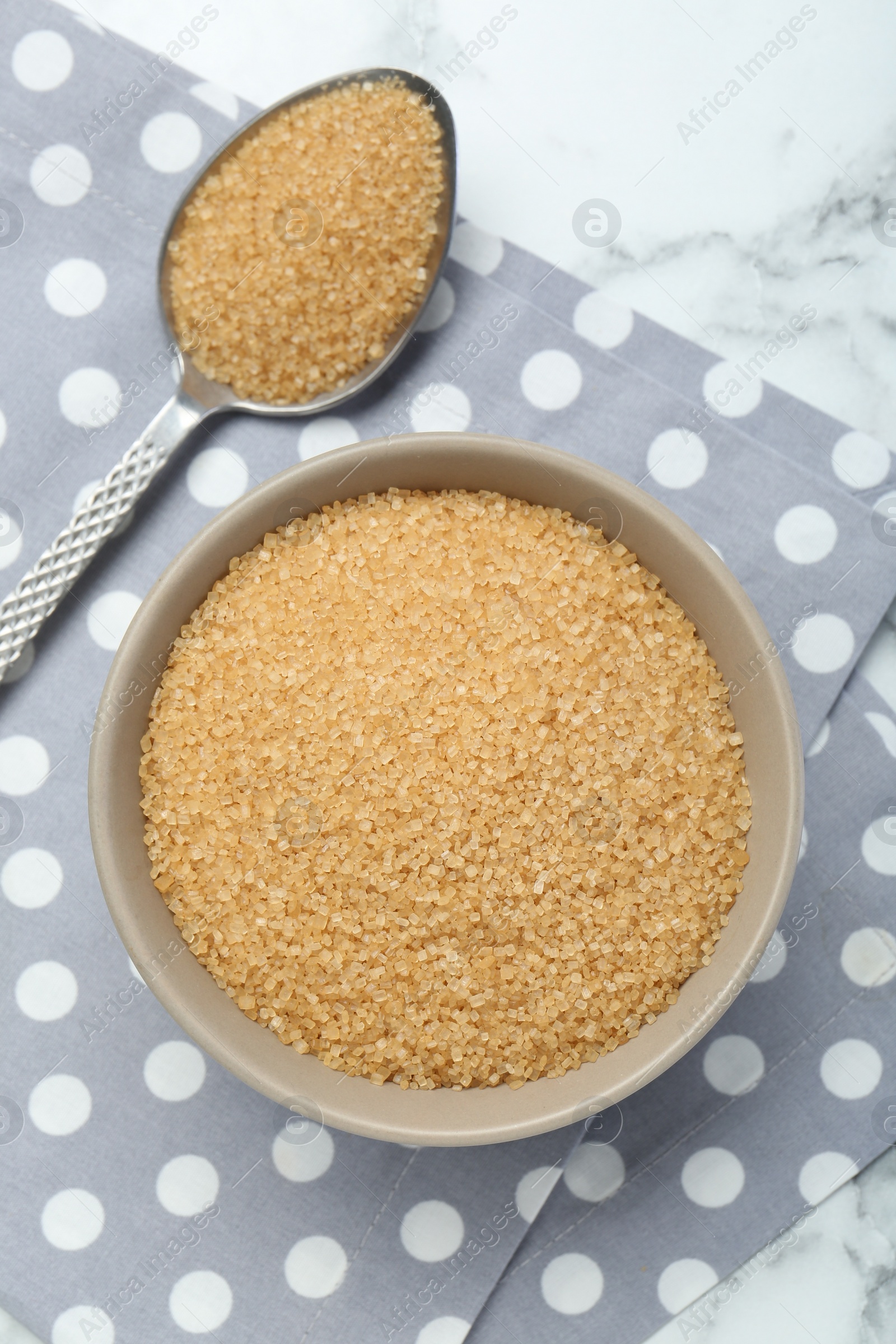 Photo of Brown sugar in bowl and spoon on white marble table, top view