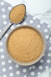 Photo of Brown sugar in bowl and spoon on white marble table, top view