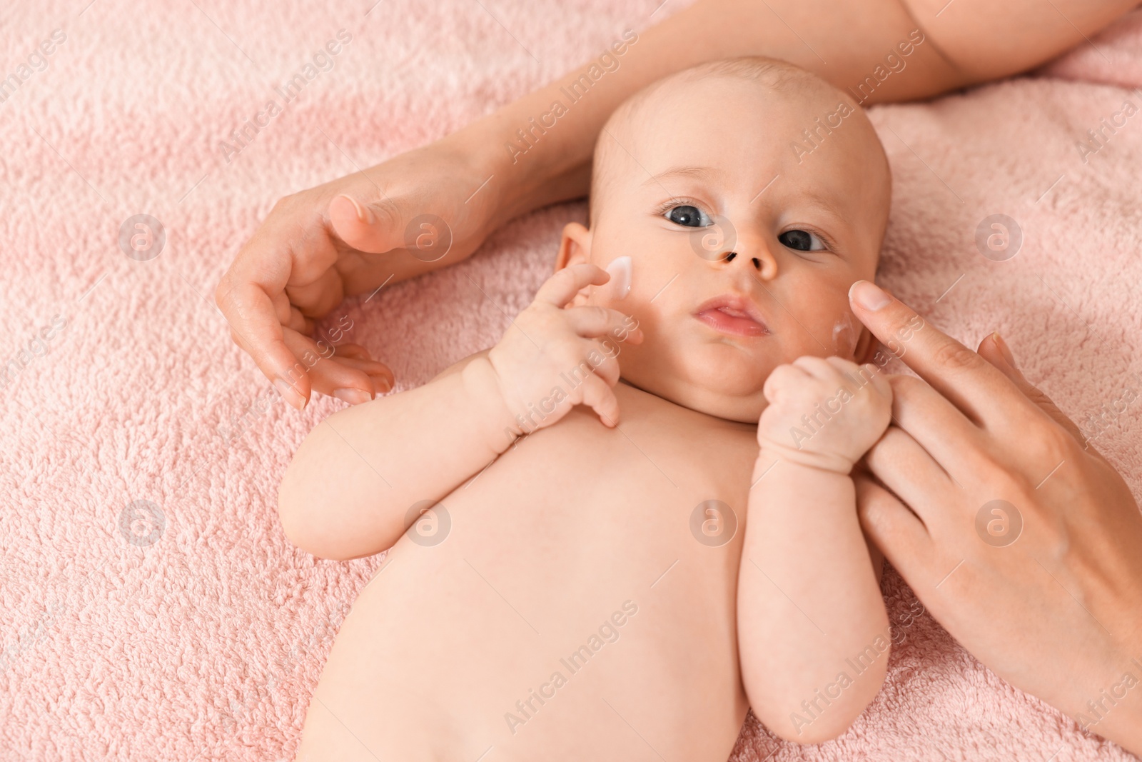 Photo of Woman applying cream onto baby`s face on bed, closeup