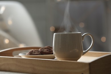 Cup of hot drink on wooden tray against blurred background, closeup