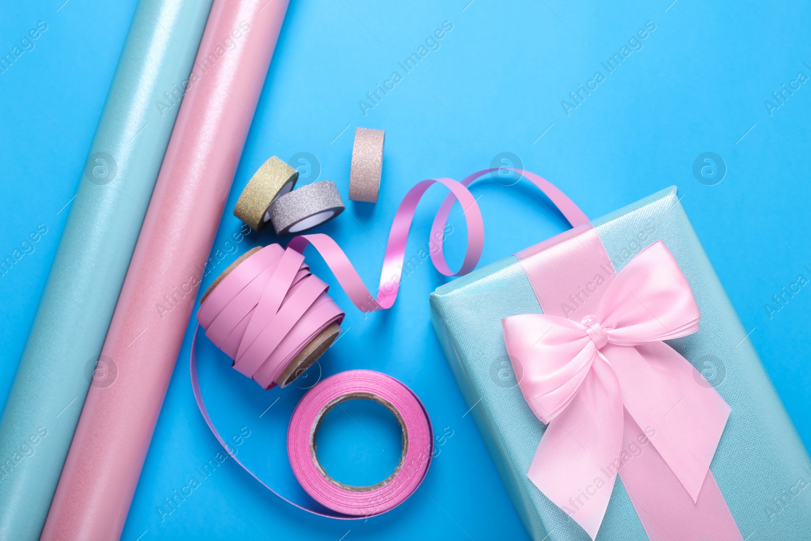 Photo of Rolls of wrapping papers, ribbons and gift box on light blue background, flat lay
