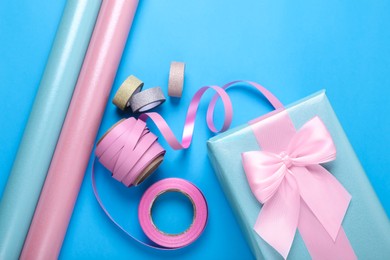 Photo of Rolls of wrapping papers, ribbons and gift box on light blue background, flat lay