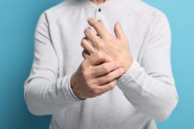 Photo of Arthritis symptoms. Man suffering from pain in hand on light blue background, closeup