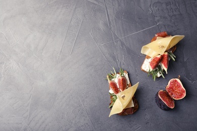 Photo of Sandwiches with ripe figs, prosciutto and cheese on grey background, top view. Space for text