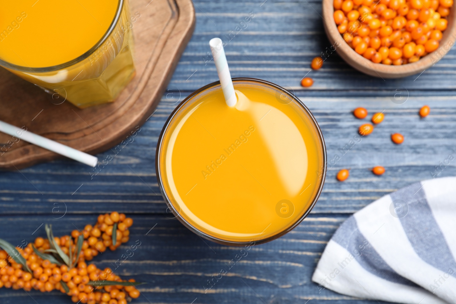 Photo of Sea buckthorn juice and fresh berries on blue wooden table, top view