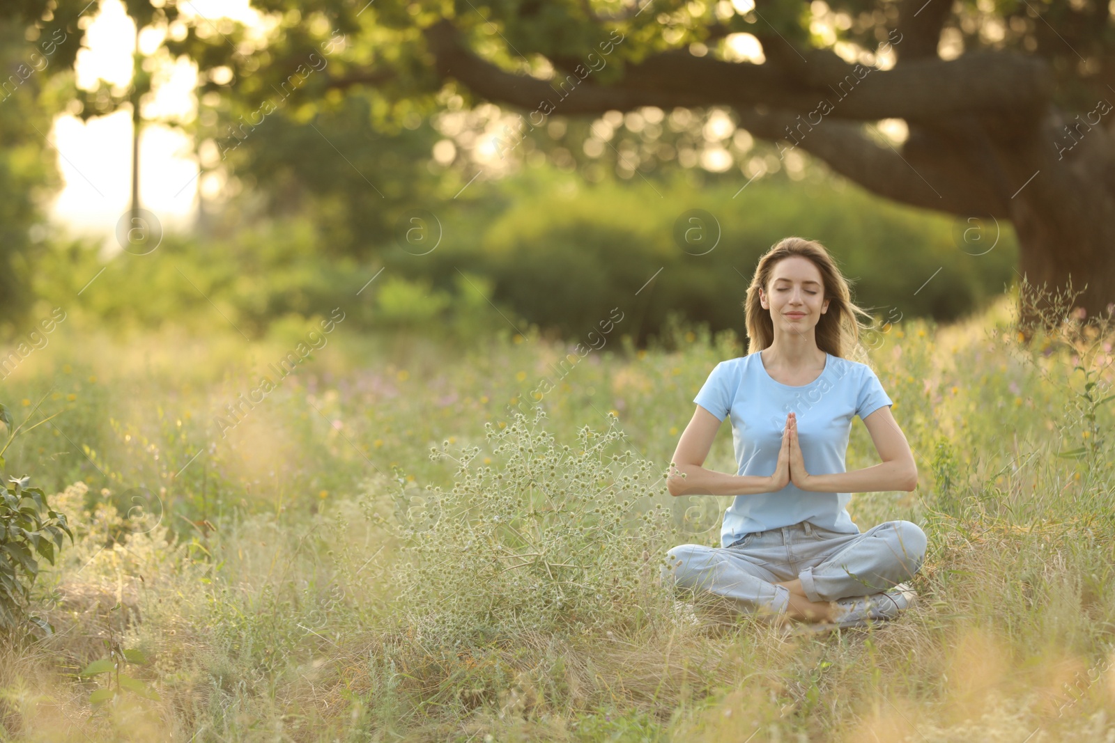 Photo of Young woman meditating on green grass in park, space for text