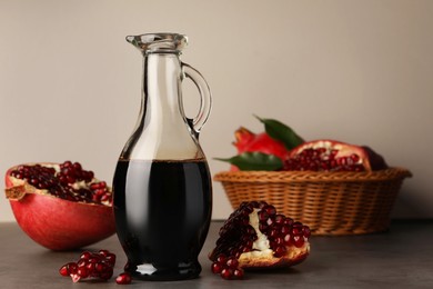 Photo of Glass jug of tasty pomegranate sauce and fresh ripe fruits on light grey table