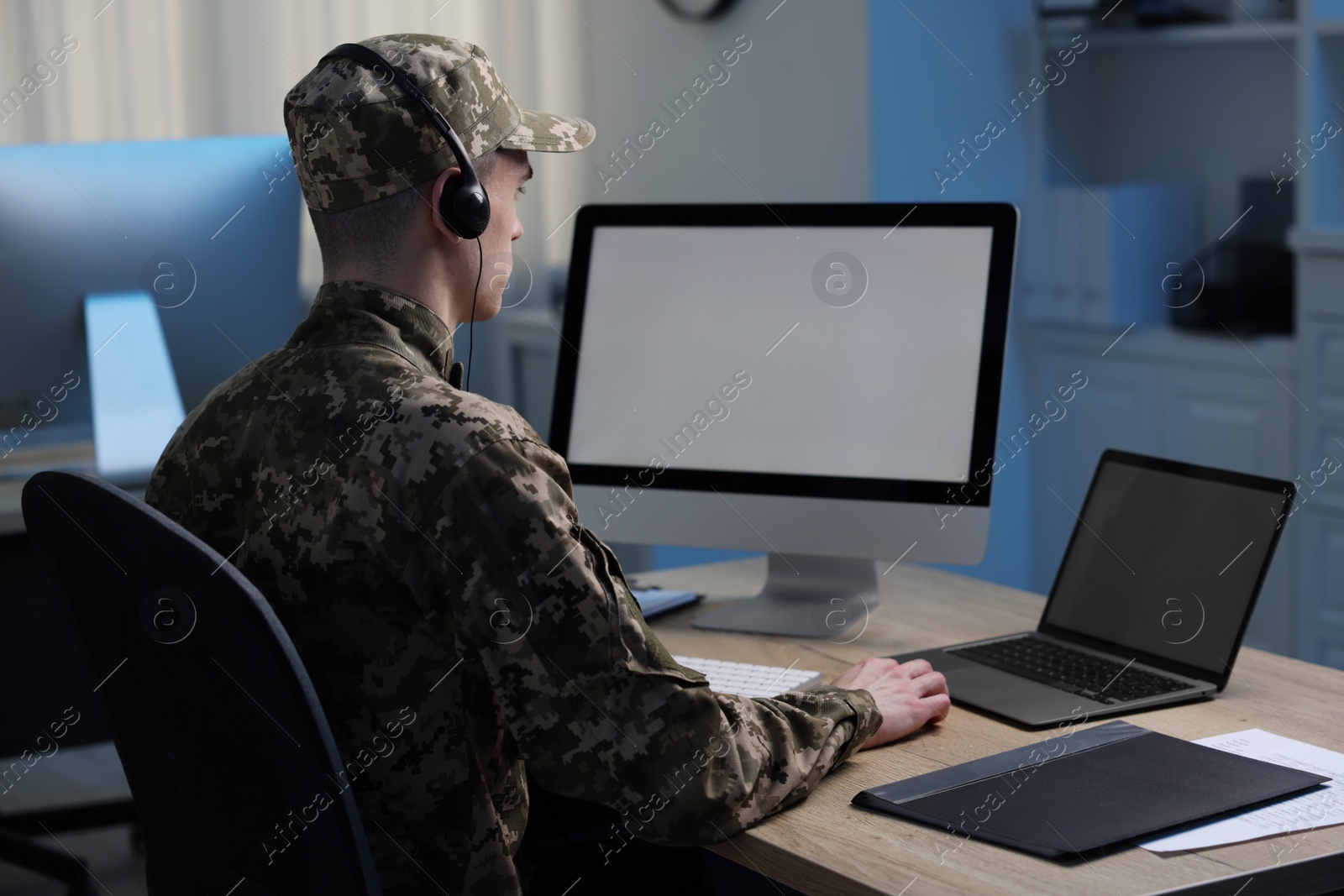 Photo of Military service. Soldier in headphones working at table in office at night