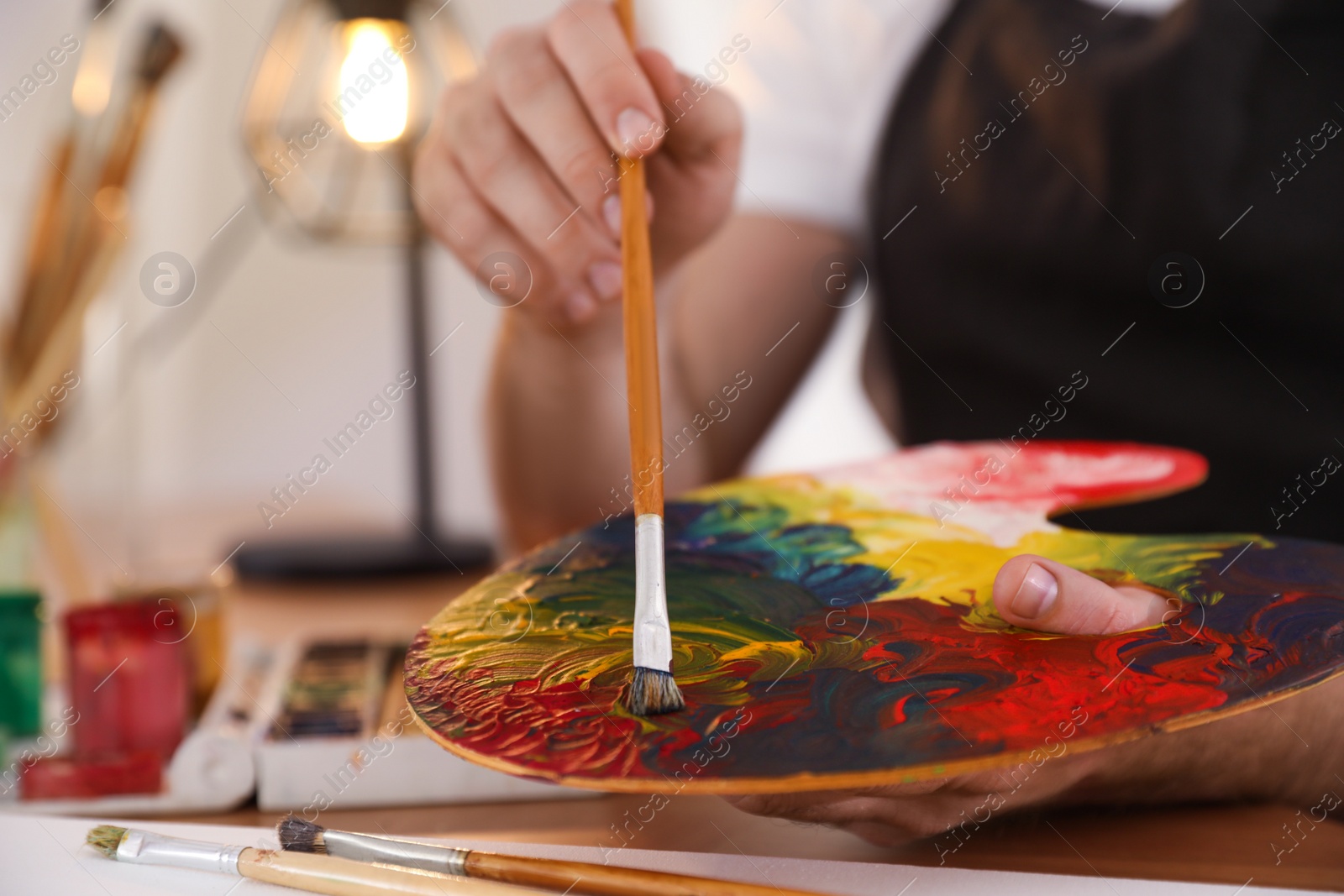 Photo of Young man with painting tools at table in artist studio, closeup