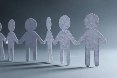 Photo of Teamwork concept. Paper figures of people holding hands on grey background, closeup