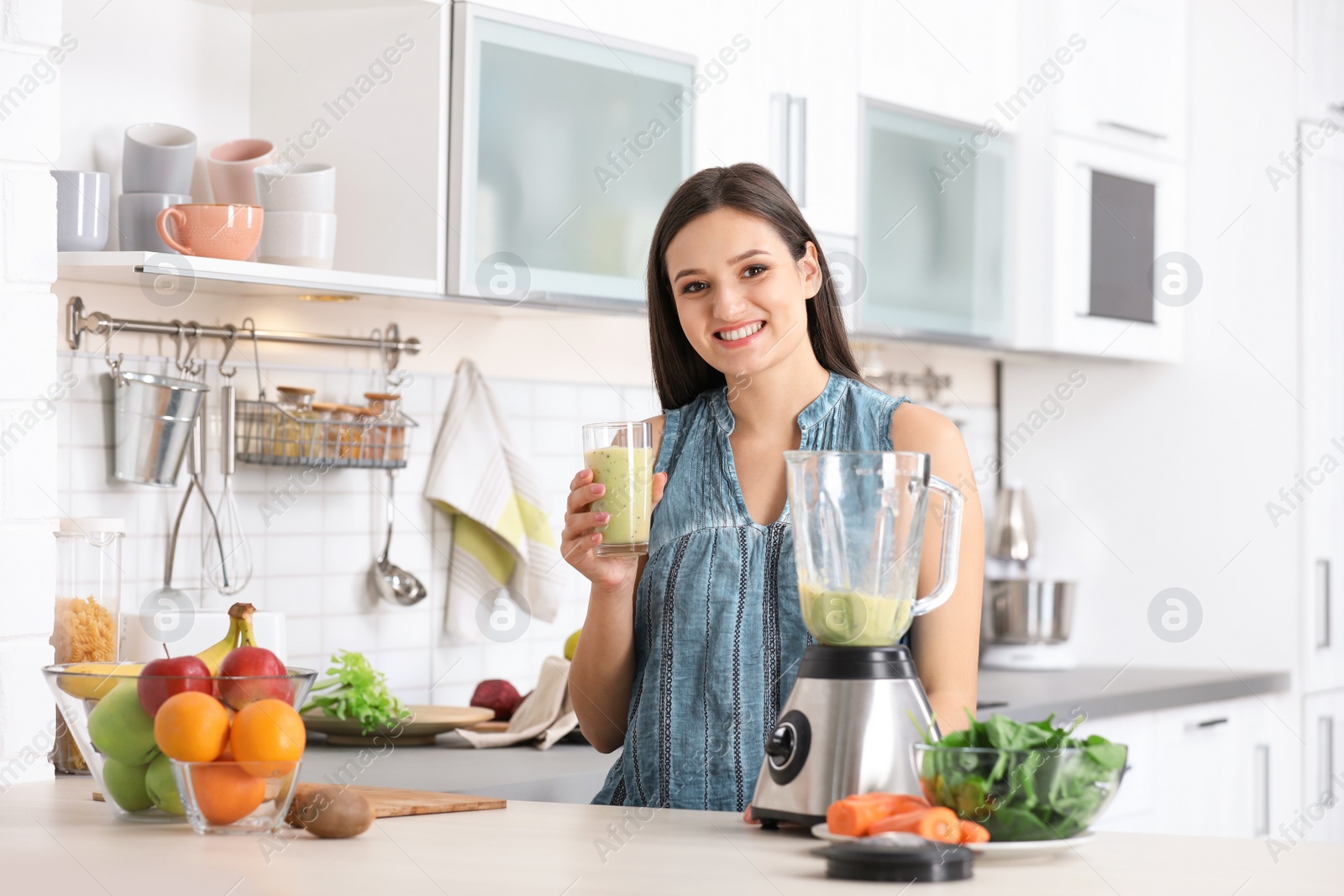 Photo of Young woman with tasty healthy smoothie at table in kitchen