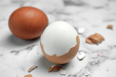 Photo of Boiled eggs and pieces of shell on white marble table, closeup