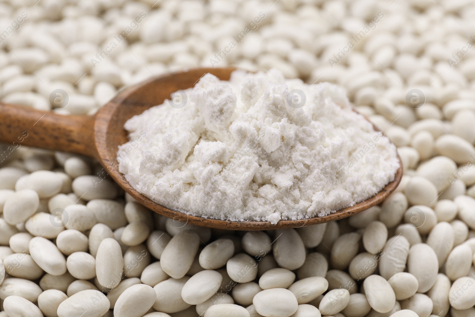 Photo of Wooden spoon with flour on white kidney beans, closeup