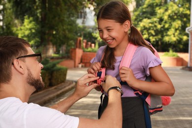 Photo of Father helping his daughter with backpack outdoors. Ready for school