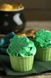 Photo of St. Patrick's day party. Tasty cupcakes with clover leaf toppers and green cream on wooden table, closeup