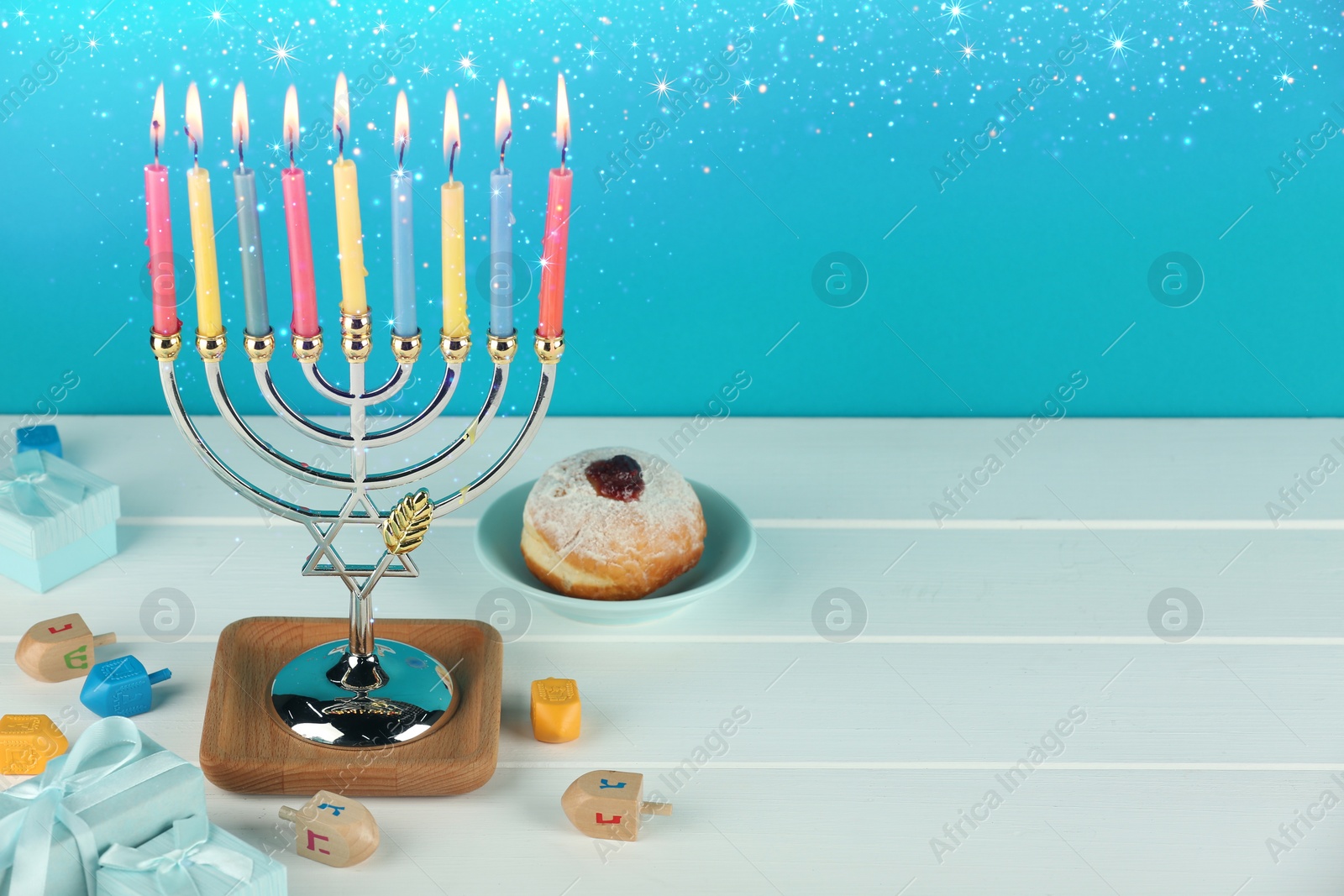 Image of Hanukkah celebration. Menorah with burning candles, dreidels, gift boxes and donut on white wooden table, space for text