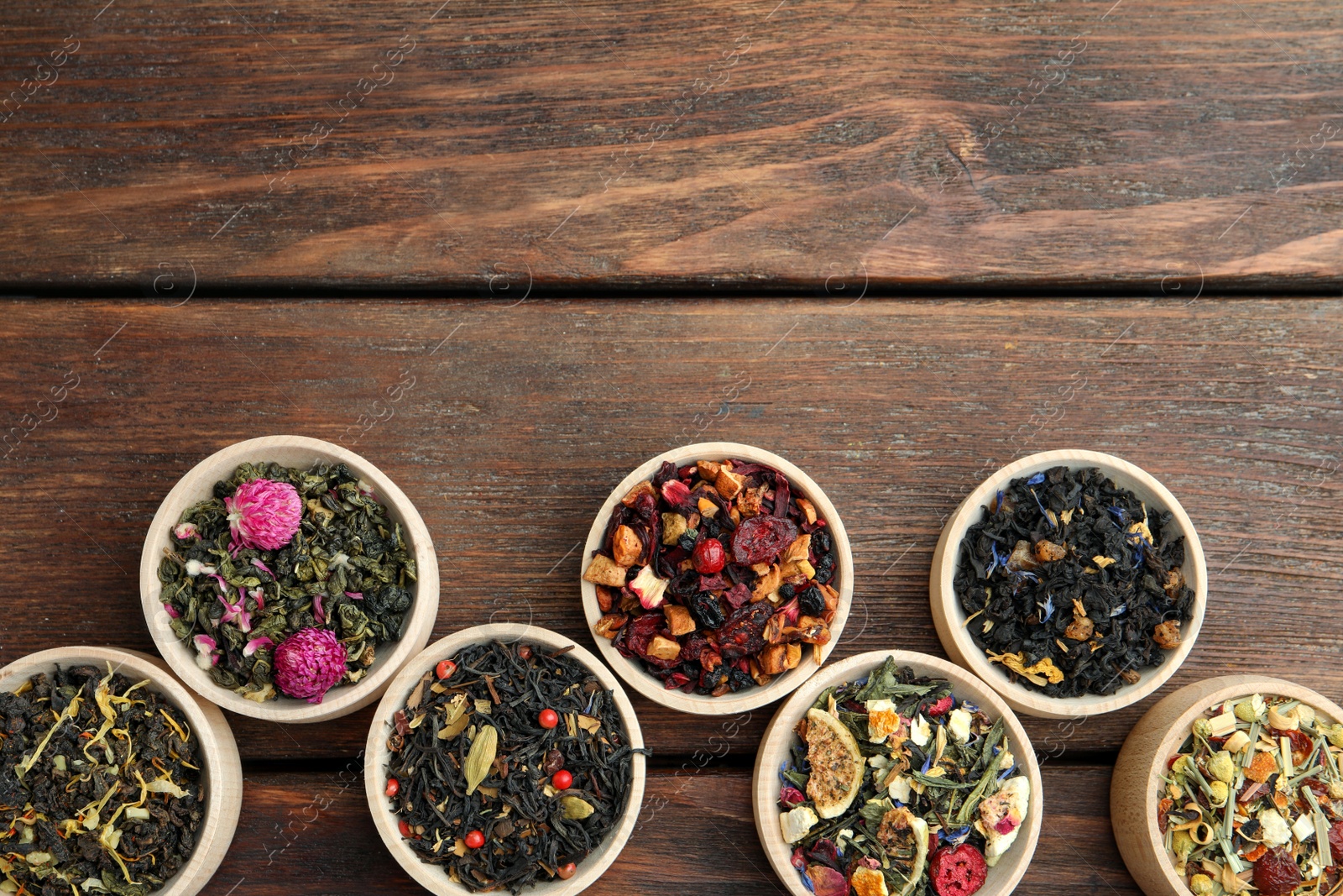 Photo of Different kinds of dry herbal tea in bowls on wooden table, flat lay. Space for text