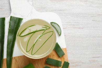 Photo of Tasty aloe juice in glass and cut fresh leaves on light wooden table, top view. Space for text