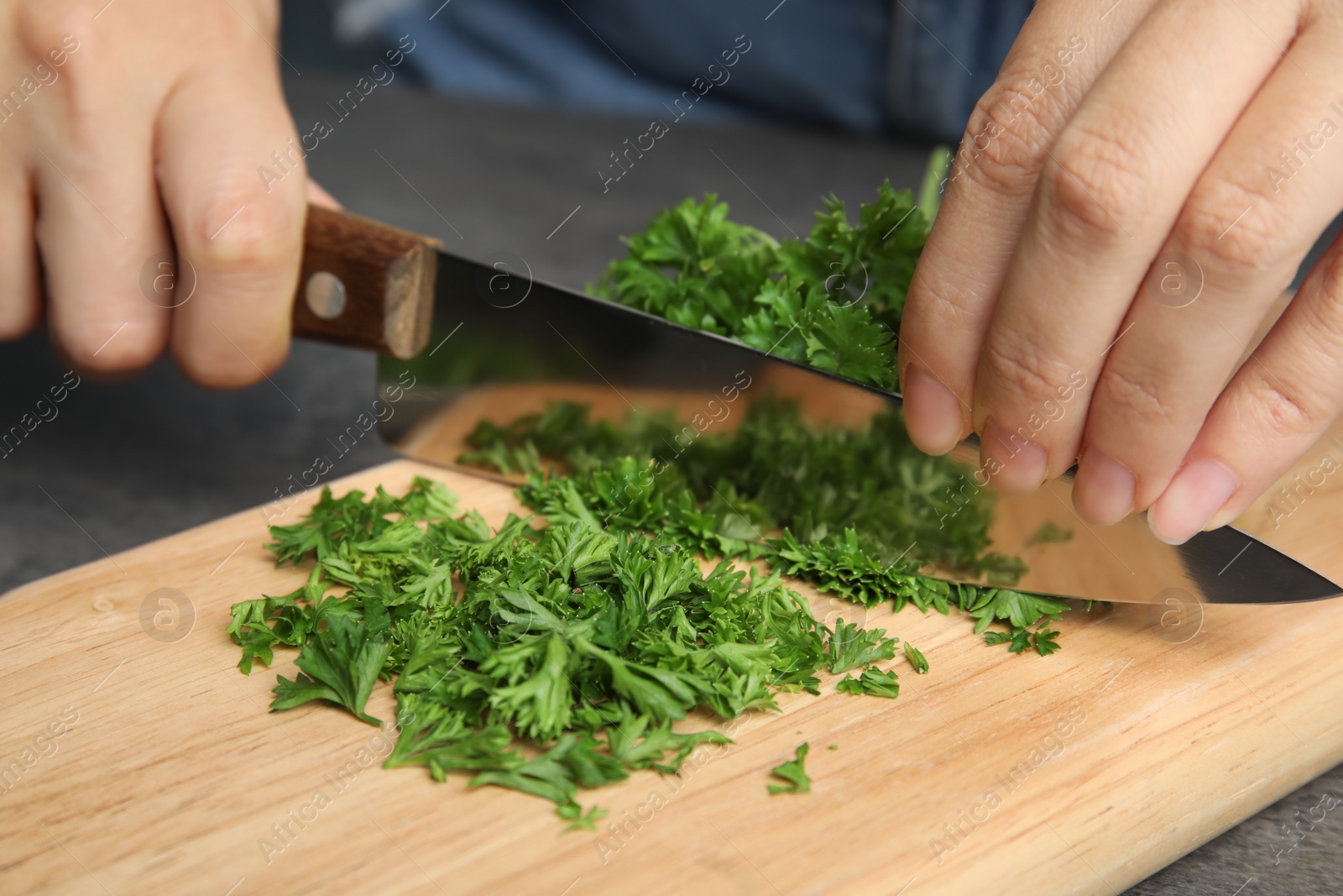 Photo of Woman cutting fresh green parsley on wooden board, closeup