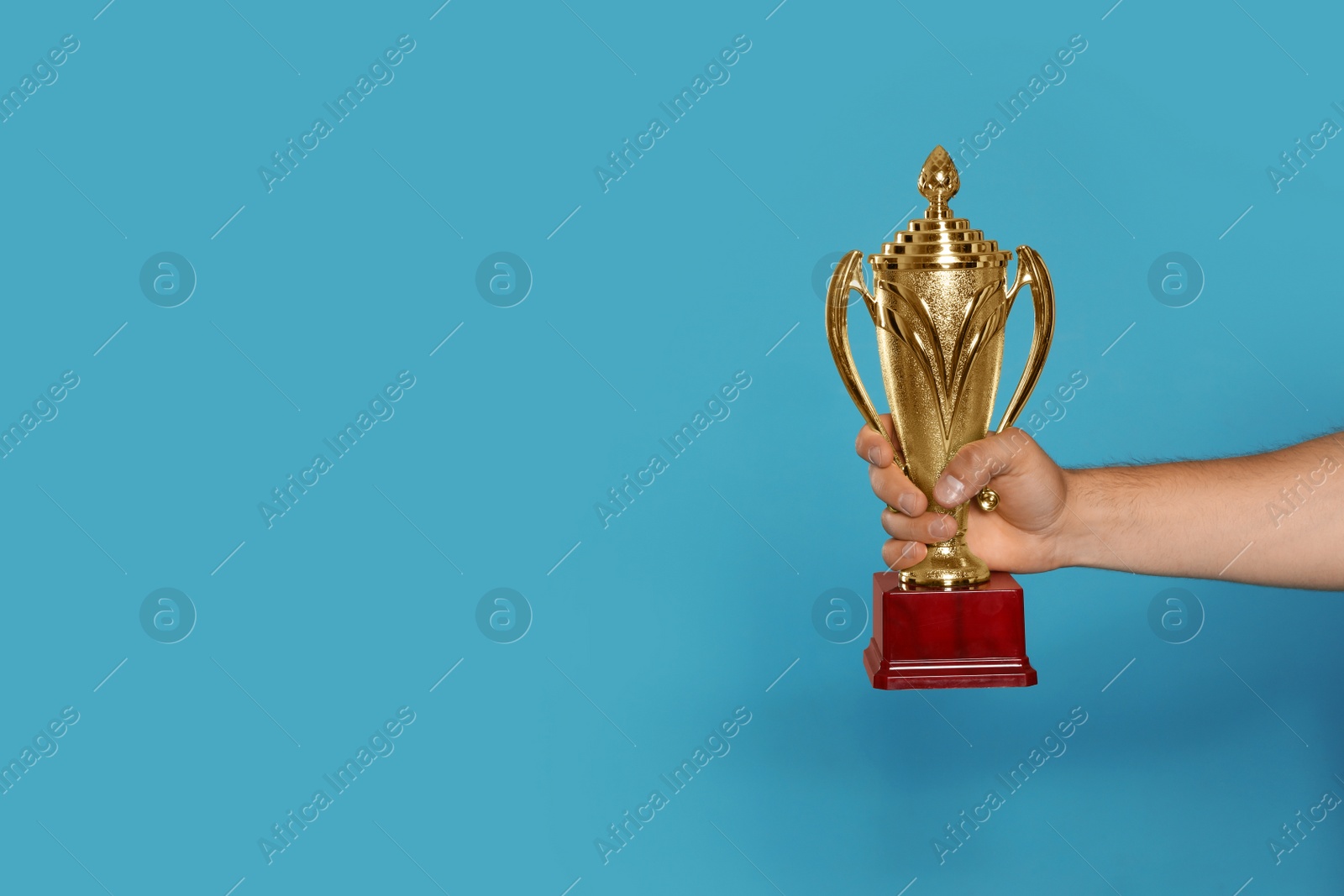 Photo of Young man holding gold trophy cup on blue background, closeup. Space for text