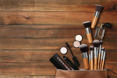 Cosmetic bag with makeup products on wooden background, flat lay. Space for text