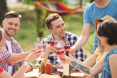 Photo of Young people with glasses of wine at table outdoors. Summer barbecue