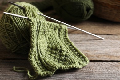 Photo of Soft green woolen yarn, knitting and needles on wooden table, closeup