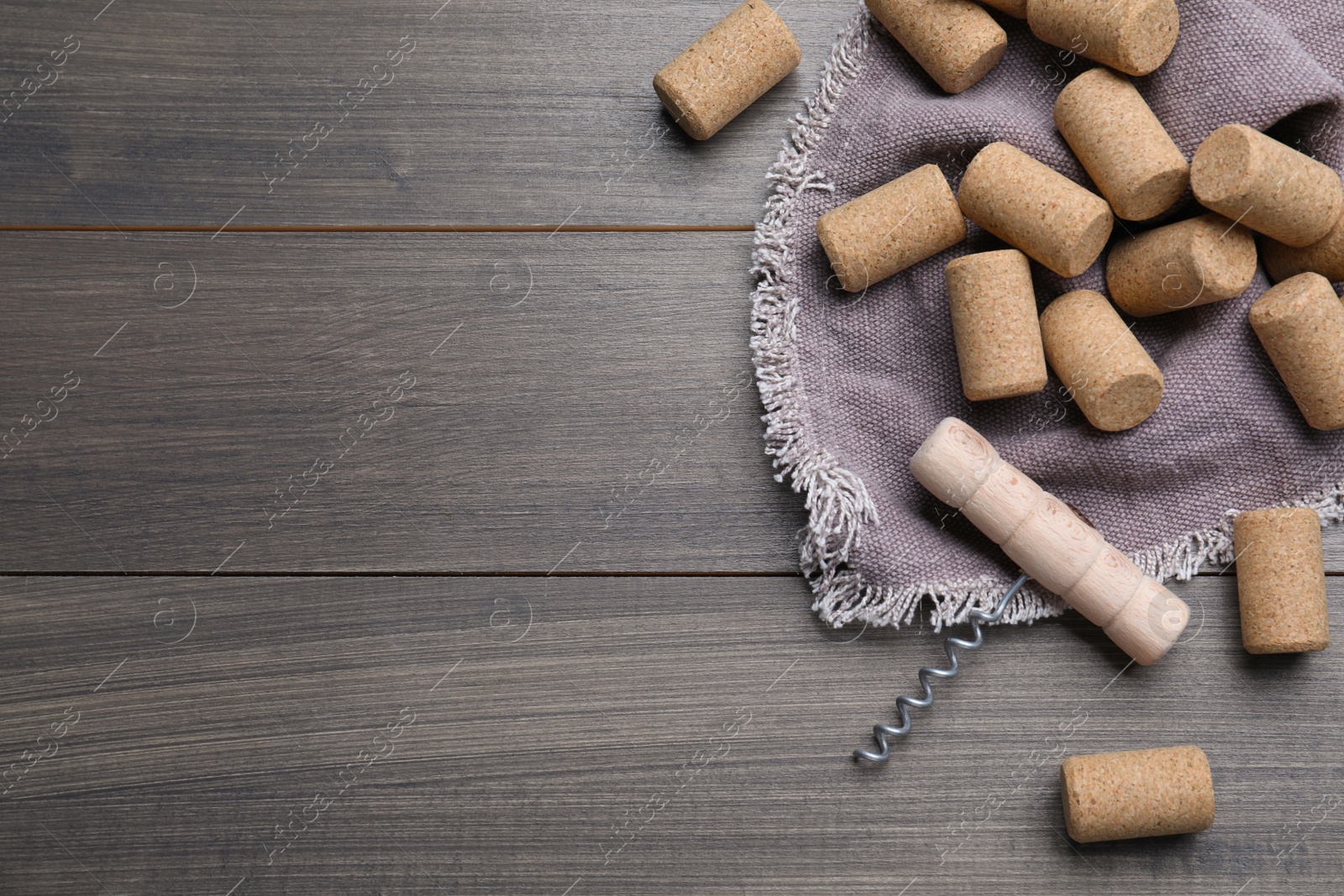 Photo of Corkscrew and wine bottle stoppers with napkin on wooden table, flat lay. Space for text