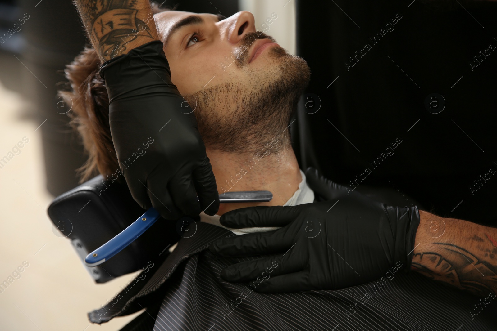 Photo of Professional hairdresser shaving client with straight razor in barbershop