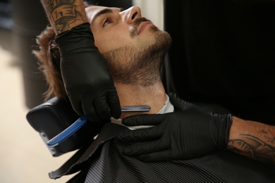 Professional hairdresser shaving client with straight razor in barbershop